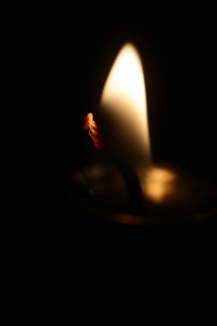 Photo closeup of single blurred soft warm flame of lighted fuse burning candlewick illuminating darkness on dark background, vertical picture